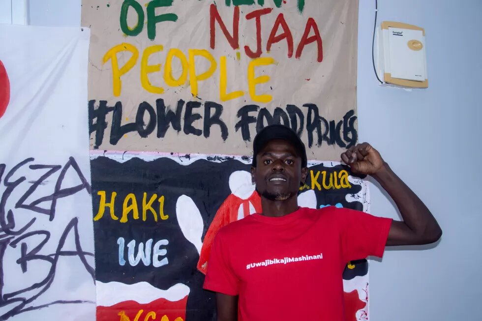 George Muhia in front of a poster demanding lower prices